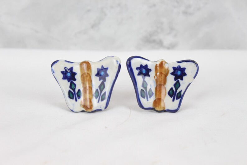 May include: A pair of ceramic butterfly-shaped drawer pulls with blue, green and brown floral designs.