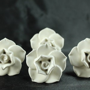 May include: Five white ceramic rose-shaped drawer pulls. Each pull features a detailed, three-dimensional rose design.