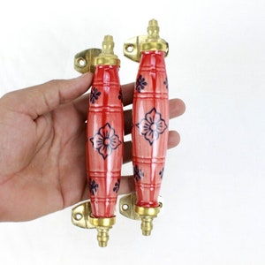 Può includere: Due maniglie per porte in ceramica rossa con un design floreale e dettagli in ottone.