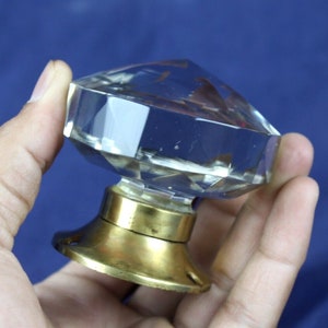 Könnte beinhalten: Ein klarer Glas-Türknopf mit einer facettierten Diamantform und einer Messingbasis.