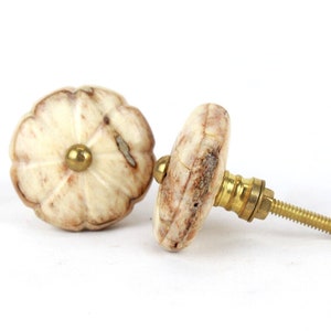 May include: Two decorative cabinet knobs made of white and brown marble with a gold metal screw. The knobs have a flower-like design.