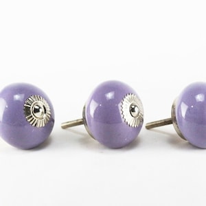 Peut inclure: Trois boutons de porte en céramique de couleur violette avec des accents argentés. Chaque bouton a une forme ronde et une vis pour l'installation.
