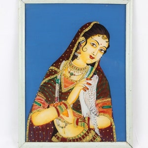May include: A framed painting of a woman in traditional Indian clothing holding a white dove. The woman is wearing a red and gold sari with a blue background.
