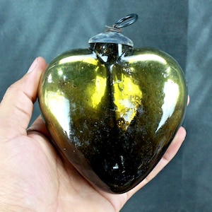 Op de afbeelding: Een donkergroene glazen hartvormige ornament met een metalen lus aan de bovenkant. De ornament is licht iriserend en heeft een vintage uitstraling.
