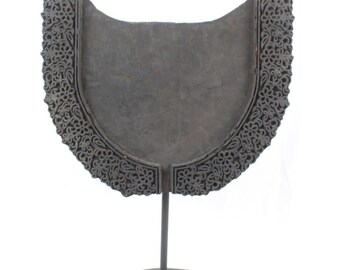 May include: A black wooden block with intricate floral carvings, mounted on a black metal stand. The block is shaped like a half-circle and has a smooth, flat surface.