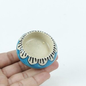 May include: A small, blue ceramic bowl with a white and black floral design around the rim.