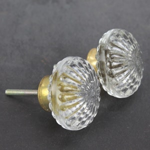 Peut inclure: Deux boutons de porte en verre transparent avec une base en laiton et un design facetté décoratif.