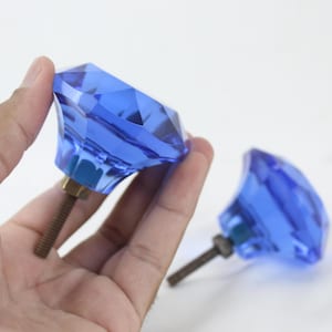 May include: Two blue glass diamond-shaped cabinet knobs with a silver metal screw.