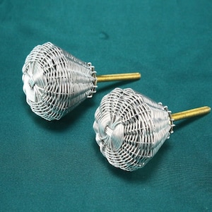 May include: Two silver wire woven cabinet knobs with a gold metal screw. The knobs are shaped like a rounded cone.