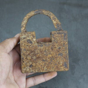 May include: A rusty padlock with a square body and a rounded top. The padlock is made of metal and has a brown and orange colour.