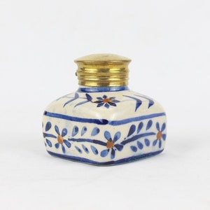 May include: A small, square ceramic inkwell with a blue and white floral design and a gold metal lid.