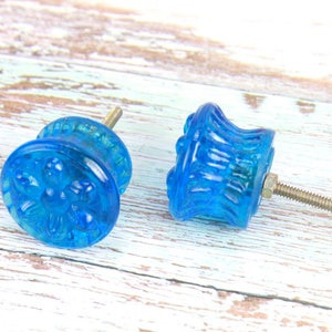 May include: Two blue glass cabinet knobs with a decorative design. One knob has a floral pattern and the other has a ribbed design.