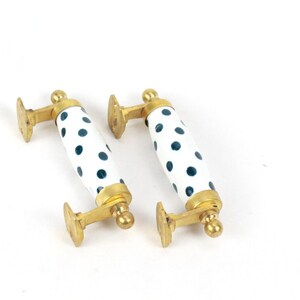 May include: Two white ceramic cabinet knobs with a black polka dot pattern and gold metal accents.