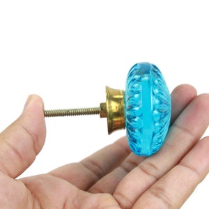 以下が含まれることがあります： クリアな水色の楕円形ガラスデザインの装飾的なキャビネットノブ。ノブは真鍮ベースと取り付け用のネジ山が付いています。ガラスにはテクスチャパターンがあります。