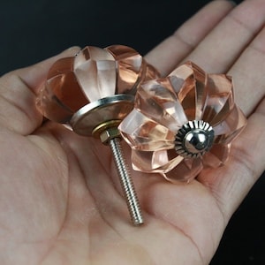 May include: Two pink glass cabinet knobs with a faceted design and silver metal accents. The knobs have a screw-on back.