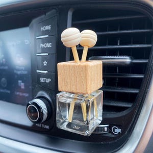Pu&ograve; includere: Un profumatore per auto con un flacone di vetro trasparente e un top a blocchi di legno. Due ornamenti a forma di palla di legno color chiaro sono attaccati alla parte superiore. Il profumatore &egrave; posto in una presa d'aria dell'auto.