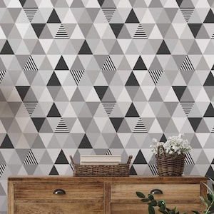 May include: A wooden dresser with six drawers and black handles sits in front of a wall covered in geometric wallpaper. The wallpaper features a pattern of black, white, and gray triangles.