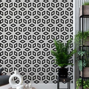 May include: A black and white geometric patterned wallpaper with a 3D effect. The wallpaper is in a living room setting with a black leather armchair, a wooden side table, and a potted plant.