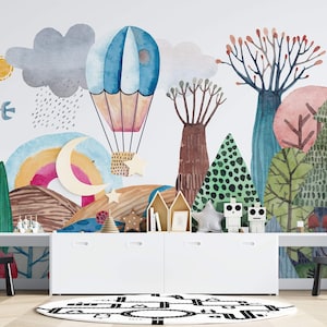 K&ouml;nnte beinhalten: Ein Aquarell-Wandbild, das eine fantasievolle Waldszene mit einem Hei&szlig;luftballon, einem Halbmond und einem Regenbogen darstellt. Zwei wei&szlig;e B&uuml;cherregale mit Schubladen flankieren einen wei&szlig;en Schreibtisch mit zwei schwarzen St&uuml;hlen.