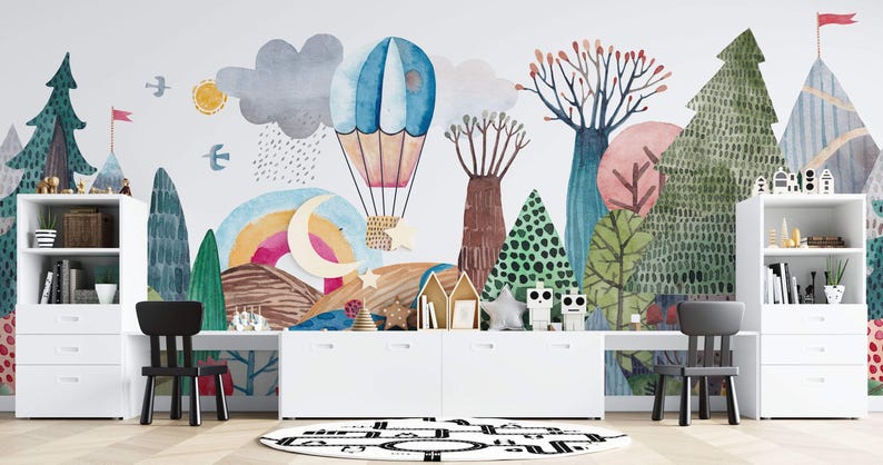K&ouml;nnte beinhalten: Ein Aquarell-Wandbild, das eine fantasievolle Waldszene mit einem Hei&szlig;luftballon, einem Halbmond und einem Regenbogen darstellt. Zwei wei&szlig;e B&uuml;cherregale mit Schubladen flankieren einen wei&szlig;en Schreibtisch mit zwei schwarzen St&uuml;hlen.
