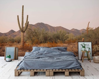 May include: A gray bed frame with a blue duvet and pillows sits in front of a desert landscape mural. The mural features a large saguaro cactus, mountains, and bushes. A framed print with the word "VIDA" is on the right side of the image.