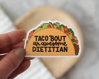 May include: A white sticker with a cartoon taco on it. The taco is filled with lettuce, tomatoes, and meat. The text on the sticker reads "Taco 'bout an awesome dietitian."