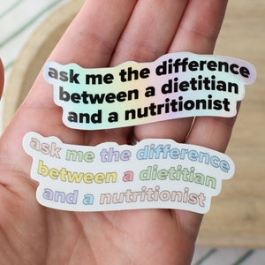 May include: Two iridescent stickers with the text "ask me the difference between a dietitian and a nutritionist" in black text.
