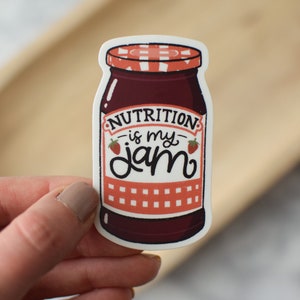 May include: A white sticker with a cartoon illustration of a jar of jam. The jar has a red and white lid and a red and white label that says "Nutrition is my jam".