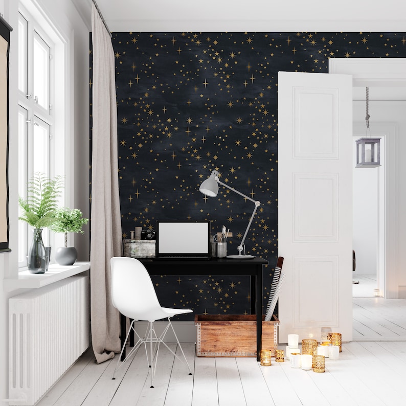 May include: A home office with a black desk and white chair. The wall is covered in a dark blue wallpaper with gold stars. A lamp is on the desk with a laptop computer. There is a wooden box on the floor next to the desk.