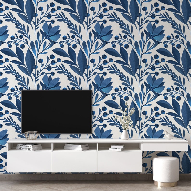 May include: A white media console with three drawers and a flat screen TV on top. The wall behind the console is covered in blue and white floral wallpaper.