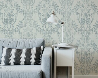 May include: A gray sofa with a black and white patterned pillow sits in front of a wall with a blue and white damask wallpaper design. A white side table holds a white desk lamp and a laptop.