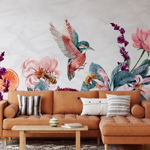 May include: Watercolor mural featuring a vibrant hummingbird with outstretched wings, surrounded by pink flowers, bees, and orange slices. A brown sectional sofa with pillows and a wooden coffee table are in the foreground.