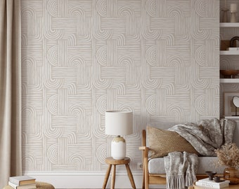 Puede incluir: Un interior de sala de estar con una pared beige con un papel tapiz de patrón geométrico blanco. Una mesa auxiliar de madera con una lámpara se encuentra frente a un sofá gris con una manta y almohadas.