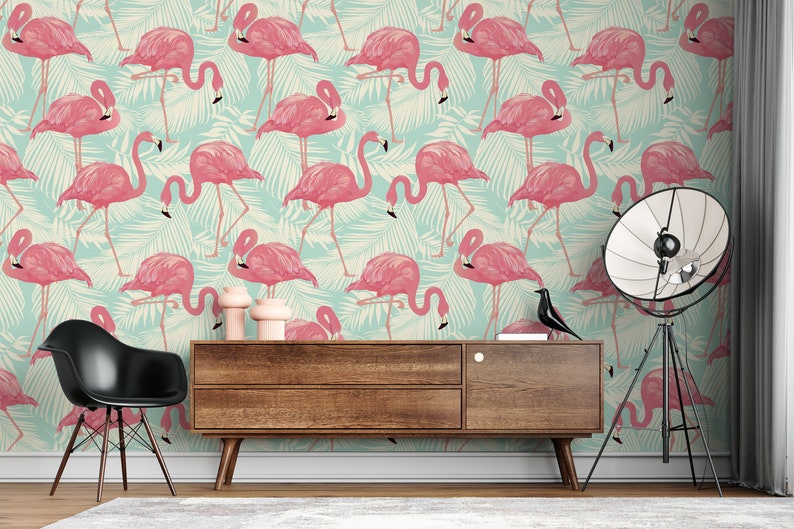 May include: A room with a flamingo-themed wallpaper. The wallpaper features pink flamingos and green palm leaves on a light blue background. A wooden cabinet, black chair, and a floor lamp are in the room.