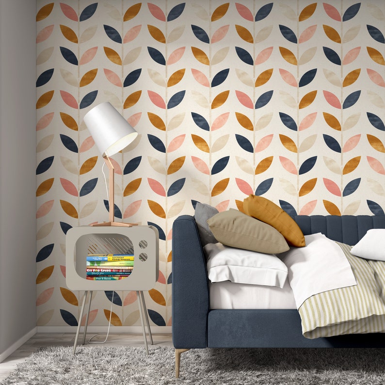Puede incluir: Una cama tapizada en azul con un edred&oacute;n y almohadas a rayas blancas y beige. La cama est&aacute; frente a una pared con un patr&oacute;n repetitivo de hojas rosas, naranjas y azules. Una l&aacute;mpara blanca con una base de madera se encuentra sobre un mueble de TV de madera con libros en su interior.