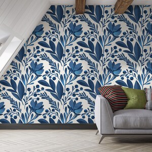May include: A white wall with a blue floral pattern wallpaper. A gray couch with pillows is in front of the wall.