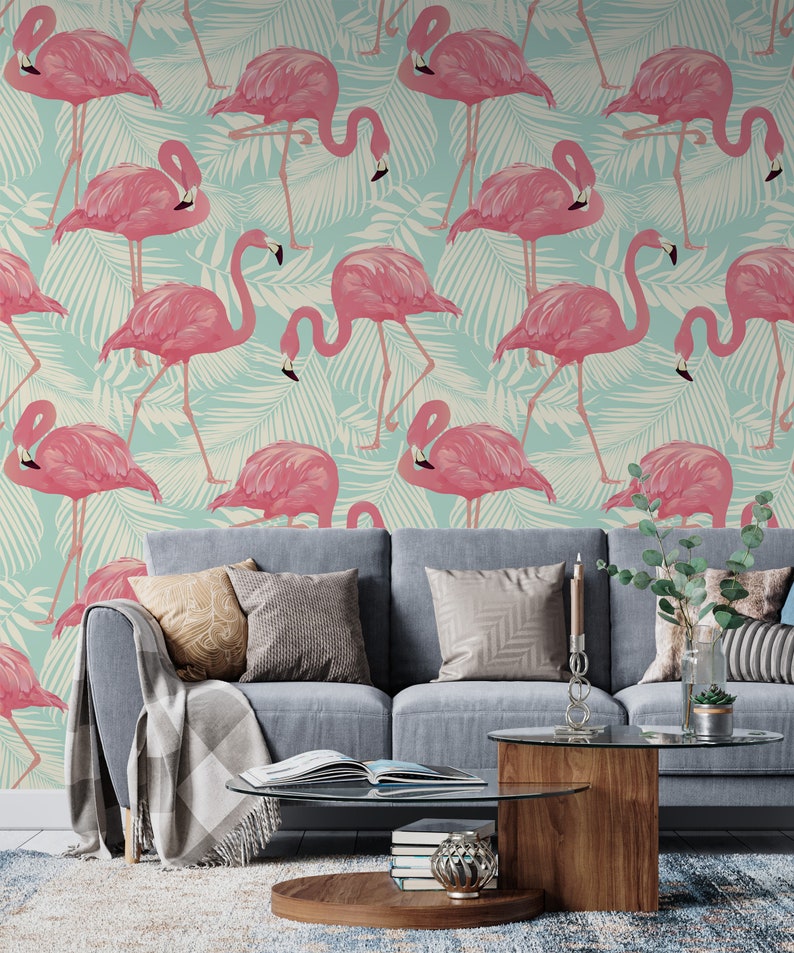May include: A living room scene featuring a light blue sofa with decorative pillows and a wooden coffee table. The wall behind the sofa is covered in wallpaper with a repeating pattern of pink flamingos and white palm leaves.