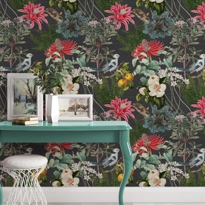 May include: A teal desk with a white stool and two framed pictures of winter scenes. The desk is in front of a wall with a dark floral wallpaper featuring birds, flowers, and leaves.