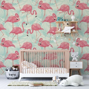 May include: A nursery scene featuring a crib with a pink and gold patterned sheet set. The wallpaper has a repeating pattern of pink flamingos on a light blue background with palm leaves. A small shelf holds toys and decorative items.