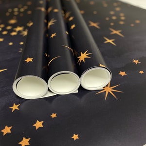 May include: Three rolls of black wrapping paper with a gold star pattern. The paper is rolled up and the ends are visible.