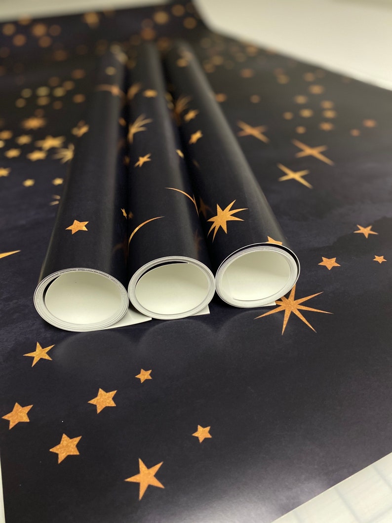 May include: Three rolls of black wrapping paper with a gold star pattern. The paper is rolled up and the ends are visible.