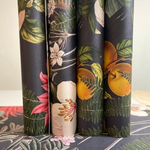 May include: Four rolls of black wrapping paper with a floral and fruit design. The paper features a variety of flowers, ferns, and fruits in shades of green, pink, white, and yellow.