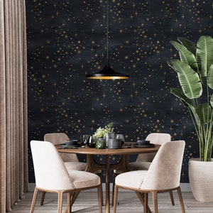 May include: A dining room with a dark blue wallpaper featuring a gold star pattern. A round wooden table with four beige chairs sits in the center of the room. A black pendant light hangs above the table.
