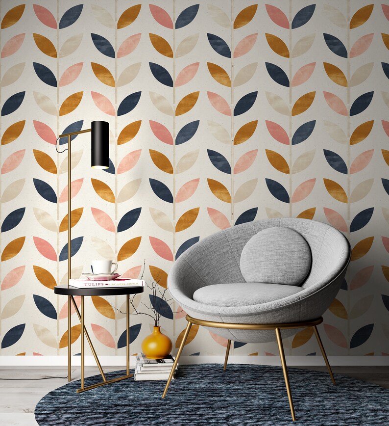 Puede incluir: Un sill&oacute;n de tela gris con respaldo redondo en forma de cuenco y patas de metal dorado. El sill&oacute;n est&aacute; delante de una pared con un patr&oacute;n repetitivo de hojas estilizadas en tonos rosa, azul y dorado.