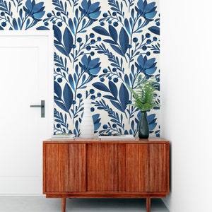 May include: A wooden cabinet with three doors, a white vase, and a potted plant. The cabinet is in front of a wall with a blue and white floral wallpaper pattern.