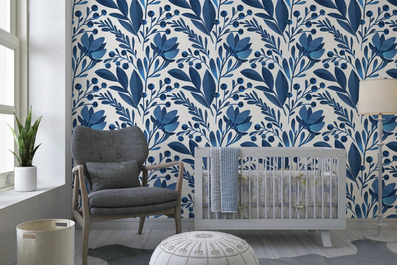May include: A nursery room with a white crib, a gray armchair, and a white ottoman. The walls are covered in a blue and white floral wallpaper.