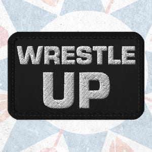 Könnte beinhalten: Schwarzer rechteckiger Aufnäher mit den Worten "WRESTLE UP" in Weiß gestickt. Der Aufnäher hat einen schwarzen Rand und ist wahrscheinlich zum Aufnähen oder Aufbügeln auf Kleidung oder Accessoires gedacht. Der Hintergrund ist ein hellblaues und weißes Muster.