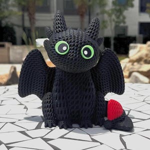 Puede incluir: Una figura de dragón negro con grandes ojos verdes y una aleta caudal roja. El dragón tiene grandes alas y está sentado sobre una superficie de baldosas blancas y grises. El dragón es un personaje de la película "Cómo entrenar a tu dragón".
