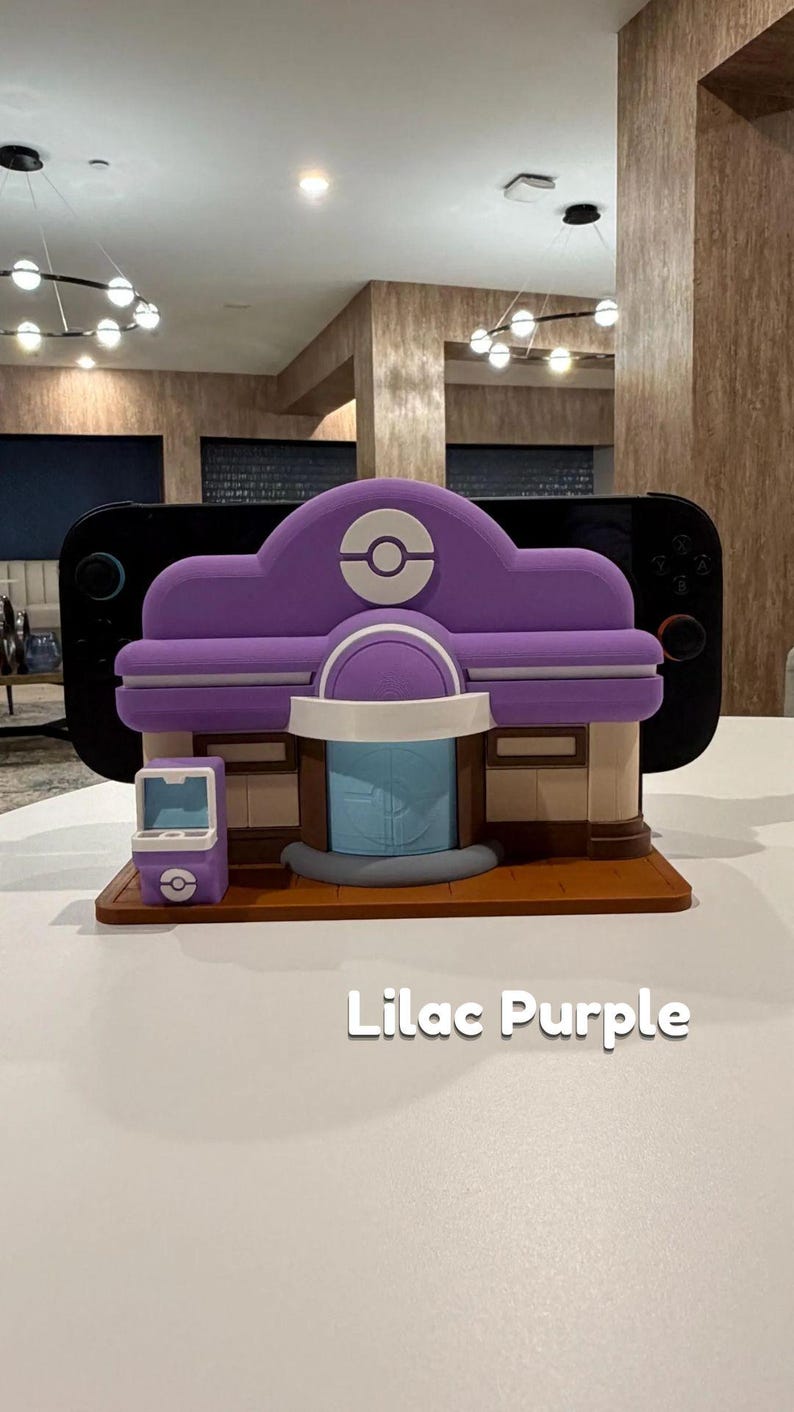 May include: A lilac purple 3D-printed model of a building with a rounded roof, a blue door, and a small matching kiosk. The model has a Pok&eacute;mon logo on the roof. The text "Lilac Purple" is below the model.
