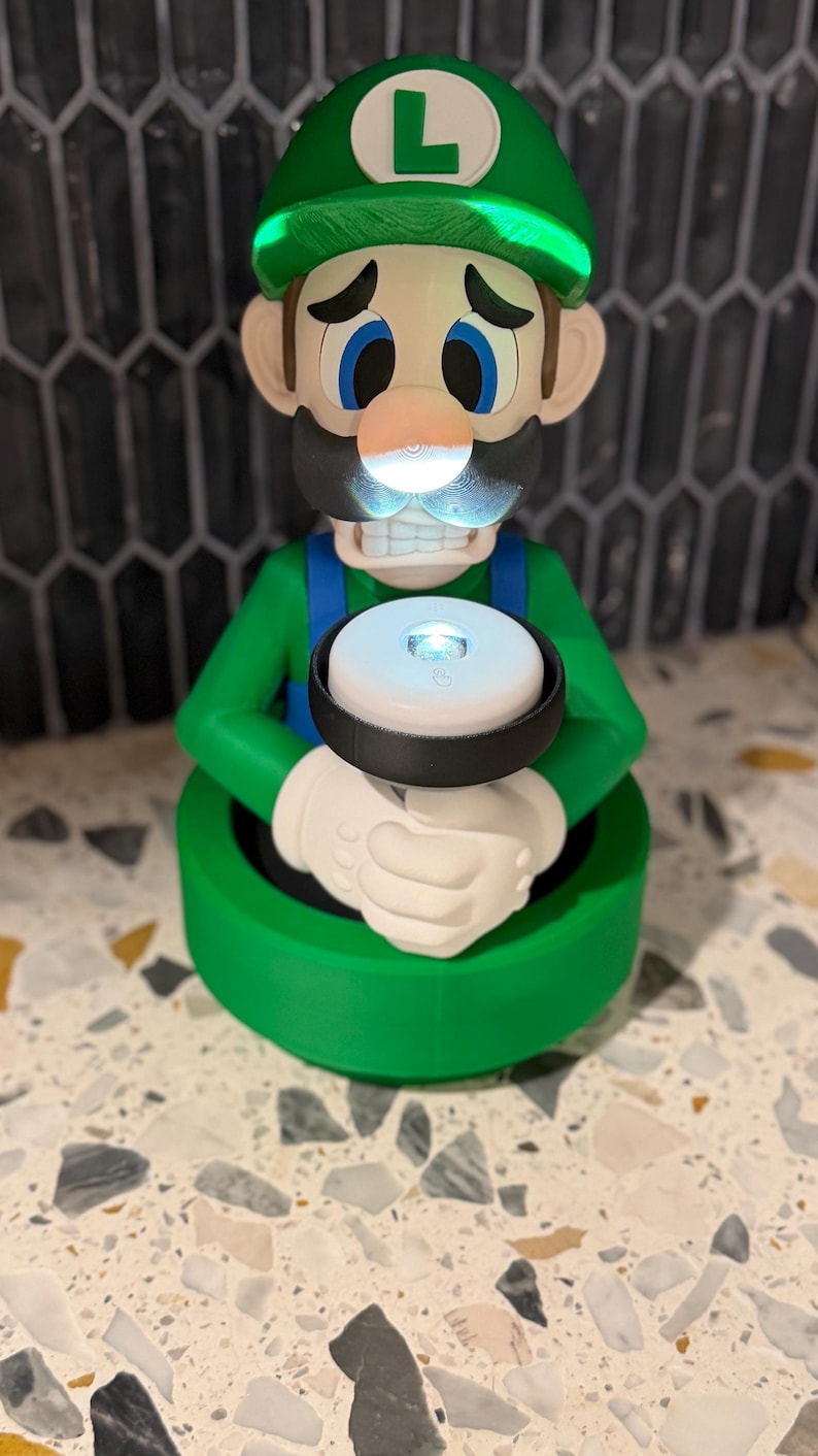 May include: A green and white Luigi figurine with a glowing light. The figurine has a green hat with a white "L" on it, blue overalls, and white gloves. The light is held in the character's hands.